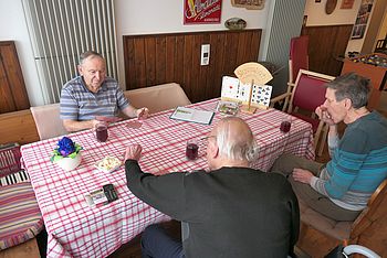 3 Männer sitzen mit Karten bei Tisch