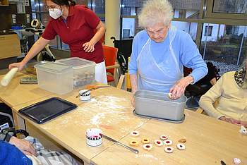 Eine Bewohnerin und eine Betreuerin packen Kekse ein.